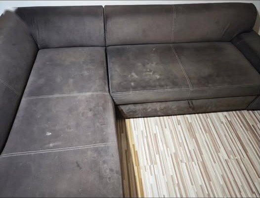 Tmavá rohová sedačka pred tepovaním — svetlé mapy a škvrny na sedákoch